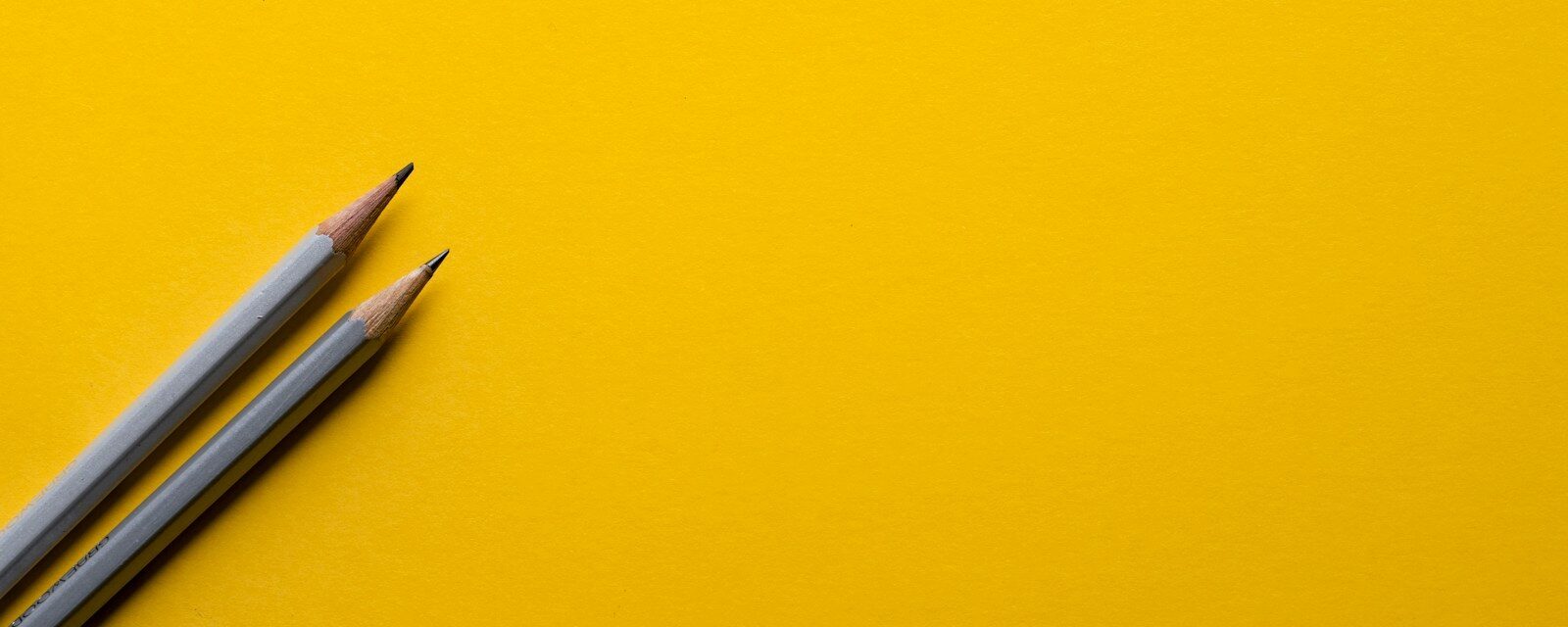 two gray pencils on yellow surface